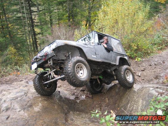 Black Jeep Wrangler with lifted suspension and large tires navigating a rocky trail