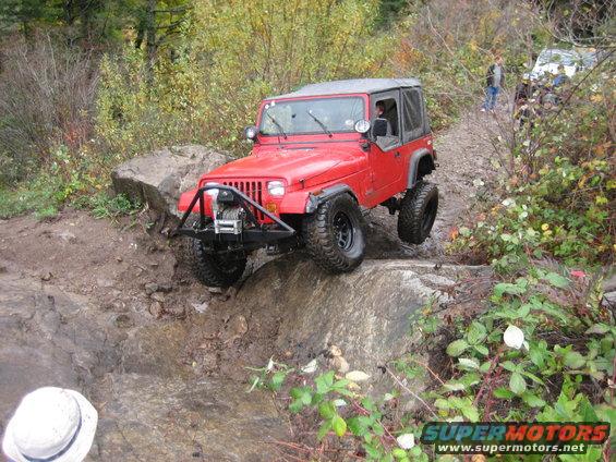 Red Jeep Wrangler navigating a rocky trail, with another vehicle visible in the background
