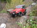 1990 Ford Bronco - A red Jeep Wrangler tackles a challenging rocky off-road course, with another vehicle partially visible further down the path.