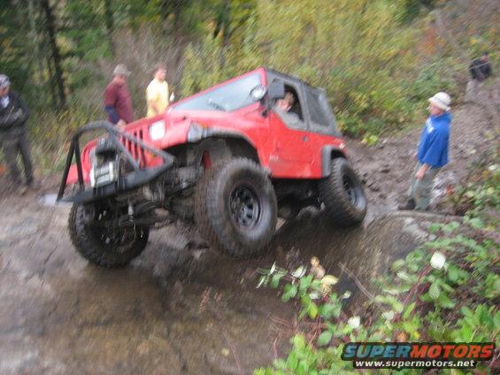 Red Jeep Wrangler going through mud and water on a trail with people watching