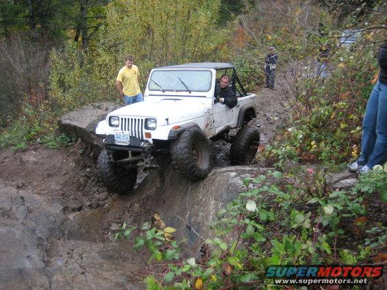 White Jeep Wrangler navigating a steep, muddy, rocky incline with people watching