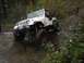1990 Ford Bronco - A white Jeep Wrangler navigates a challenging off-road course with muddy terrain and large rocks.