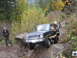 1990 Ford Bronco - A dark-colored Ford Bronco navigates a challenging off-road course with onlookers present.