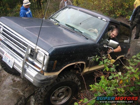 1990 Ford Bronco navigating rocks on an off-road trail, driver visible
