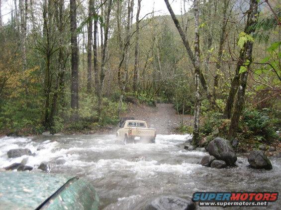 Tan Toyota pickup truck crossing a rocky stream in a forest