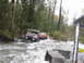 1990 Ford Bronco - Two off-road vehicles are seen navigating a river in a wooded area.