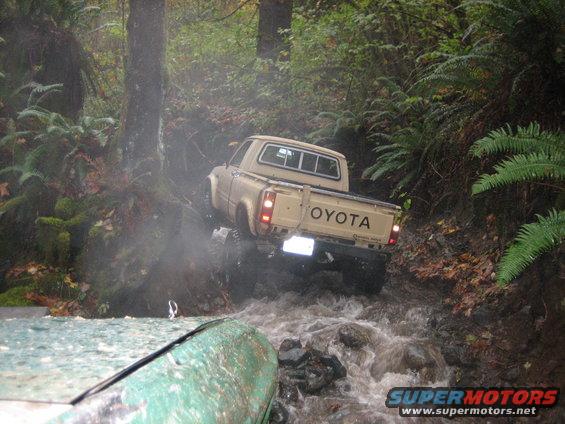 Toyota pickup truck navigating a rocky stream, another vehicle partially visible in foreground