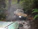 1990 Ford Bronco - Toyota pickup truck driving through a stream in a wooded area. Another vehicle is in the foreground.