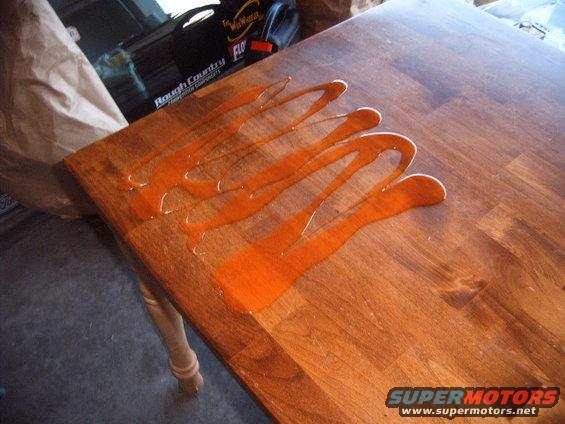 Wood table with orange liquid poured on it, part of a table leg visible