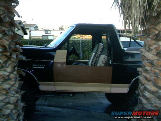 Side view of a black 1989 Ford Bronco with tan trim and a removable top. The doors are off