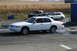 1997 Mercury Grand Marquis - A white sedan performs a burnout on a paved surface, with a field of dry crops in the background.