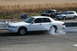 1997 Mercury Grand Marquis - White 1997 Mercury Grand Marquis performing a burnout on a track, with other vehicles visible.