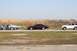 1997 Mercury Grand Marquis - A line of vehicles, including a maroon sedan, a white SUV, and two older cars, are parked on the side of a road with a cornfield behind the…