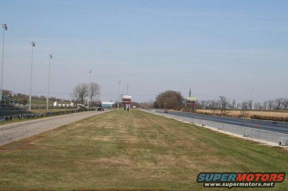 Drag strip with bleachers, lights, and a few cars on the track