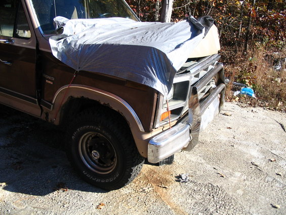 1984 Ford Bronco front quarter view, covered with a tarp. The vehicle has a chrome bull bar and is parked outdoors