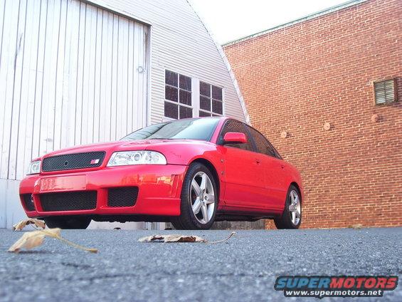 Red 1997 Audi A4 sedan, front 3/4 view, parked on asphalt near brick building