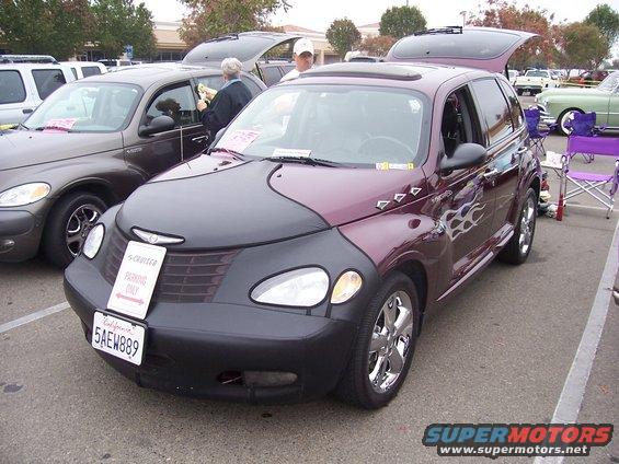 Maroon Chrysler PT Cruiser with a black car bra and flame decals, parked at an outdoor event
