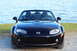 2006 Mazda Miata - A black 2006 Mazda Miata convertible is shown from the front, parked near a body of water.
