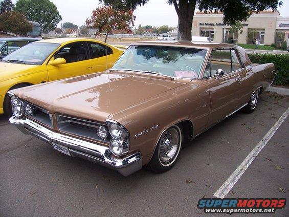 Brown 1963 Pontiac Grand Prix parked next to a yellow car. The Grand Prix has a chrome grille and bumper
