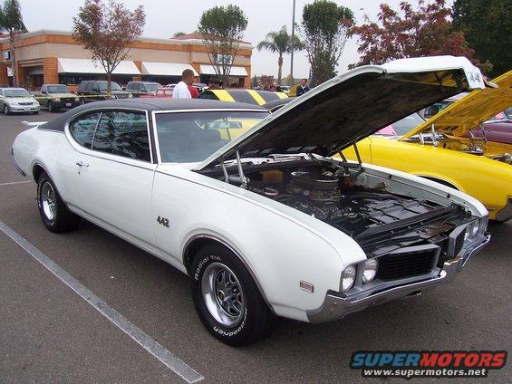 White 1969 Oldsmobile 442 with hood open, parked next to a yellow car
