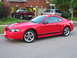 2003 Ford Mustang - A red 2003 Ford Mustang coupe is parked in front of a suburban house with two trucks and an SUV in the driveway.