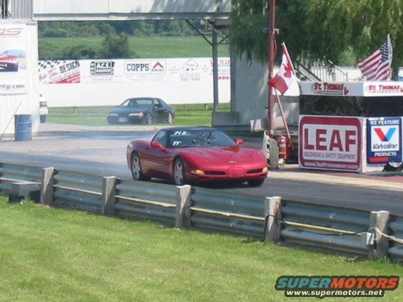 Red Chevrolet Corvette on a drag strip with a black car in the background
