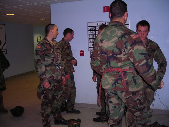 Military personnel in camouflage uniforms stand near a whiteboard with text