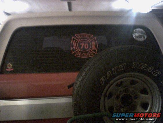 Rear window of a vehicle with a fire department sticker and a spare tire