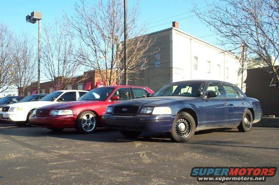 Several Ford Crown Victoria police cars parked in a lot. One is dark blue, others are red and white