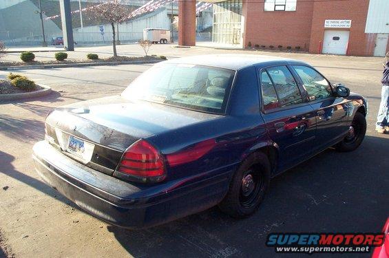 Dark blue 2001 Ford Crown Victoria sedan, rear 3/4 view, black steel wheels, some paint damage on trunk lid