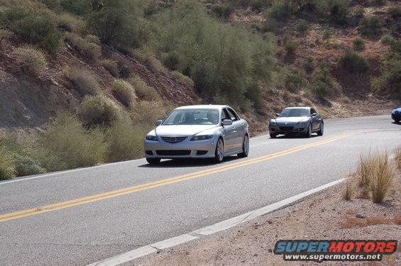 Silver sedan and gray coupe on a desert road, with Supermotors logo