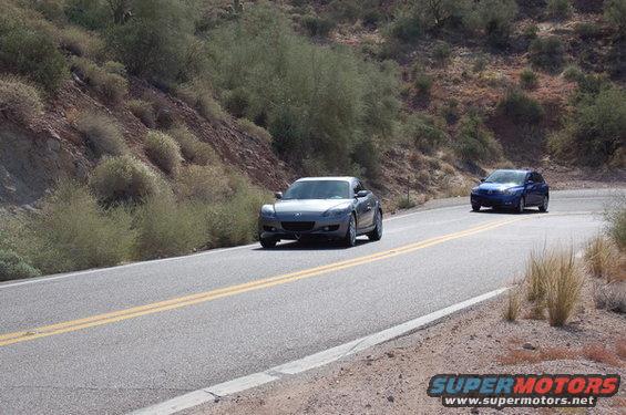 2006 Mazda RX-8 and a blue sedan driving on a two-lane road through a desert landscape