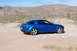 2006 Mazda RX-8 - A blue 2006 Mazda RX-8 is seen from a three-quarter front view, parked on a dirt road with a desert mountain range in the background.