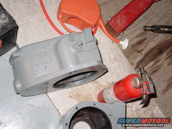 Gray metal automotive part with casting numbers C-11871 and D, next to a fire extinguisher and orange watering can