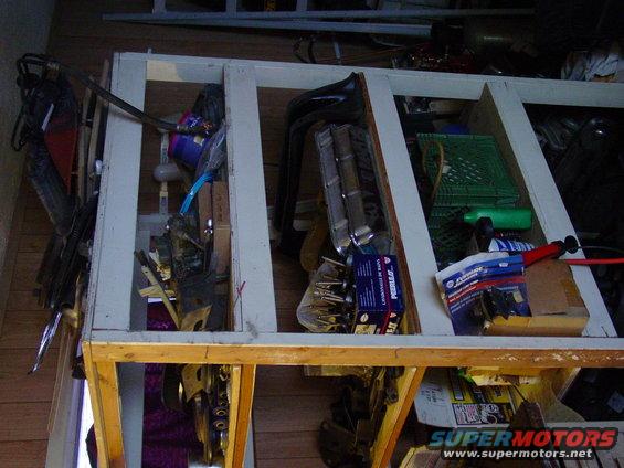 Various automotive parts stored in a wooden rack, including what appears to be a grille and other metal components