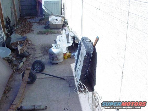 Radiator leaning against a wall next to a propane tank and various parts