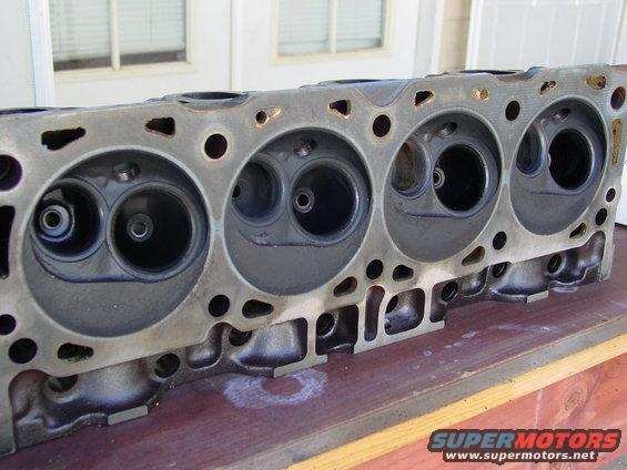 Engine cylinder head with four pairs of intake and exhaust ports, resting on a wooden surface