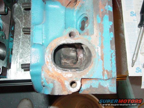 Close-up of a teal-painted engine cylinder head with rust and wear around a large opening