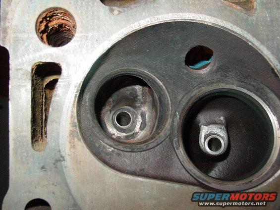 Engine cylinder head with two valve openings, one showing carbon buildup and the other clean
