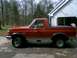 1989 Ford Bronco - This red Ford Bronco, likely from the late 1980s, is parked in front of a residential garage.