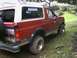 1989 Ford Bronco - This red Ford Bronco is parked off-road, showing its rear quarter panel and spare tire.