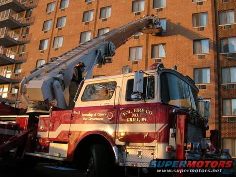 Fire truck with ladder extended towards a building. Text on door reads 'VOL. FIRE CO. NO. 1 GRILL, PA'