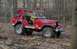 1989 Ford Bronco - A red Jeep CJ-series vehicle, modified as a fire truck, drives through a wooded area with a firefighter at the wheel.