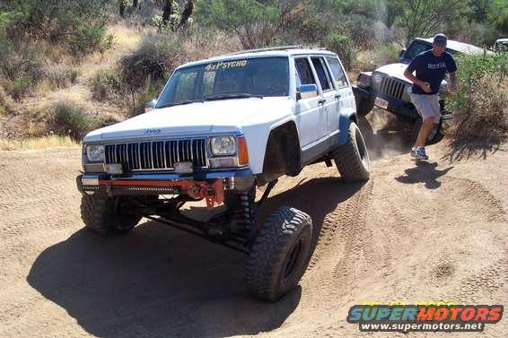 White Jeep Cherokee XJ with "4XPSYCHO" decal on windshield, lifted suspension, off-roading