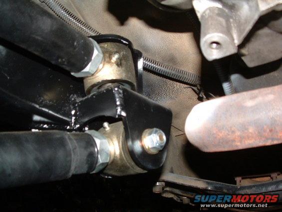Close-up of a suspension component with bolts and metal brackets. Supermotors.net logo visible