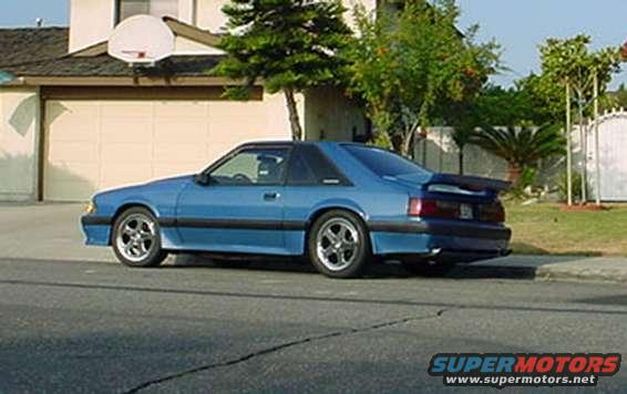 Blue coupe car parked on street, side view. Has a rear spoiler and aftermarket wheels