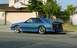 1988 Ford Mustang - A blue coupe car with a rear spoiler is parked on the street in front of a garage.