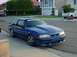 1988 Ford Mustang - A blue Ford Mustang is parked on the side of the road in front of a house and garage.