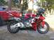 1993 Ford Probe - A red Honda sportbike is parked next to a red pickup truck, with a helmet on its handlebars.