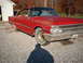 1961 Ford Starliner - A red vintage car with a distinctive grille and chrome accents sits on a gravel lot under a clear sky.